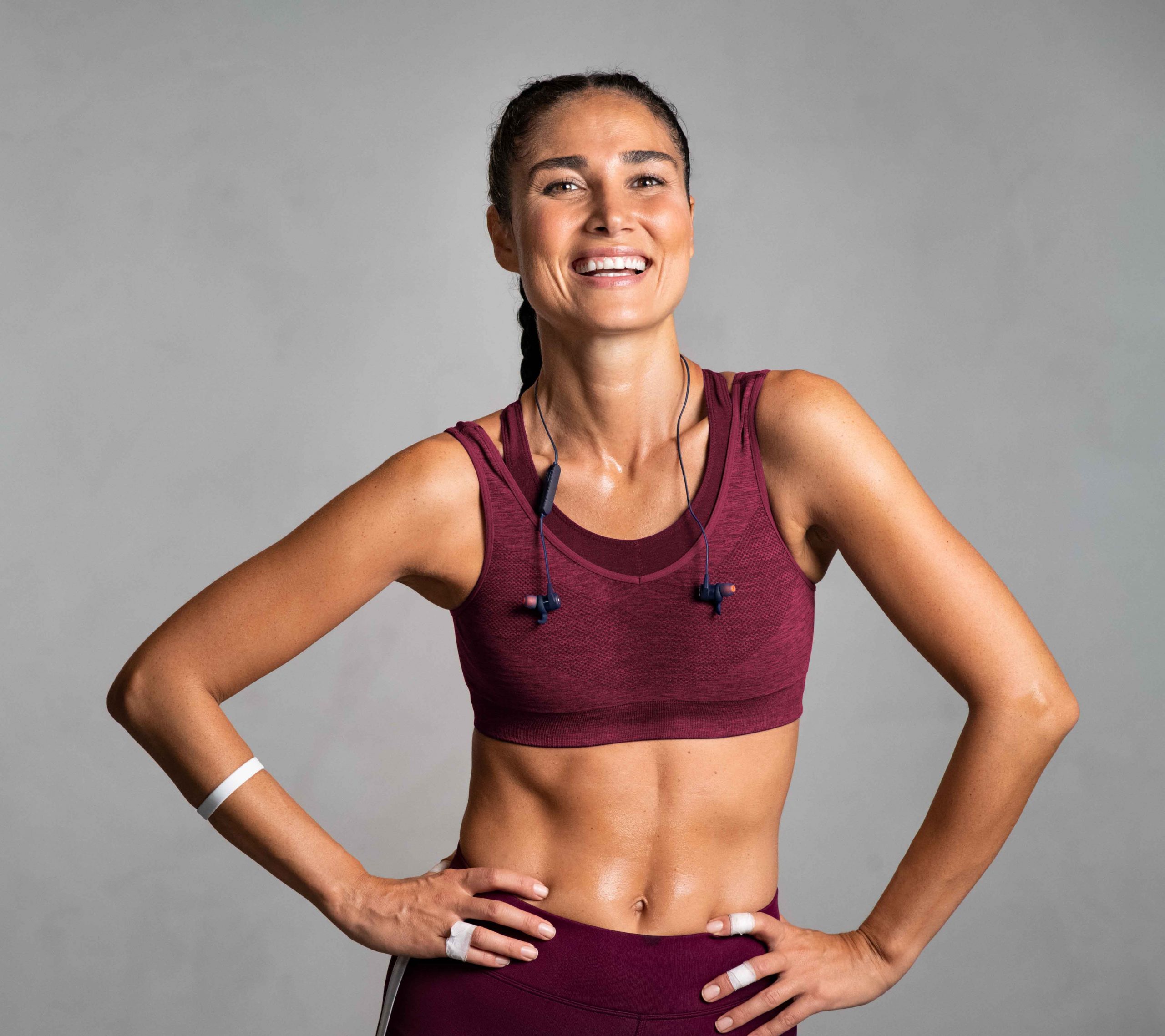 Portrait of beautiful fitness woman smiling and looking at camera isolated on grey background. Mid woman in sportswear relaxing after training at gym. Happy fit girl on gray wall with copy space.